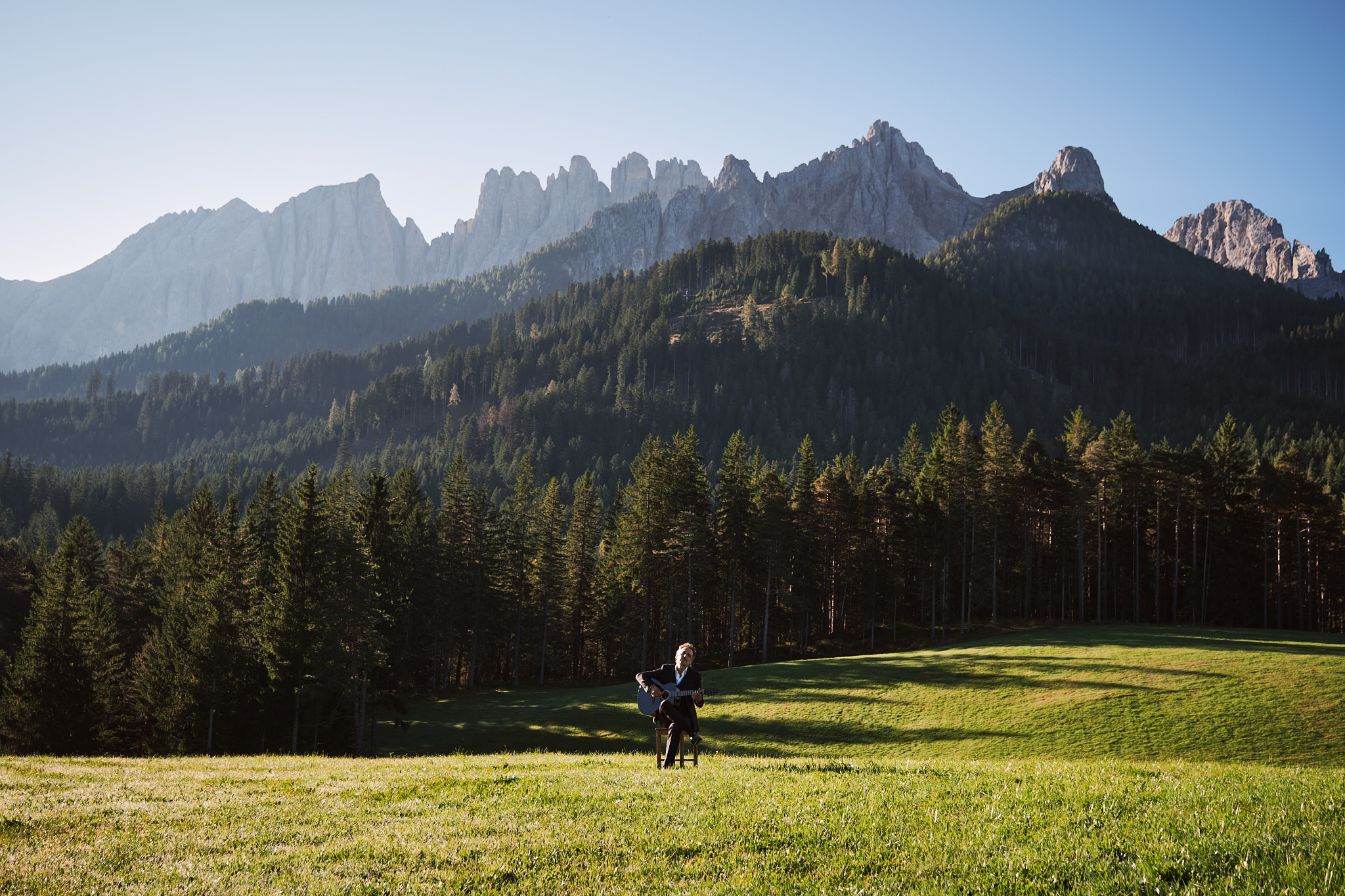 Guitarist playing a Thom Orgler Latemar acoustic (PU high-gloss Smokegrain) outdoors in the Dolomites, eyes closed, enjoying the performance.