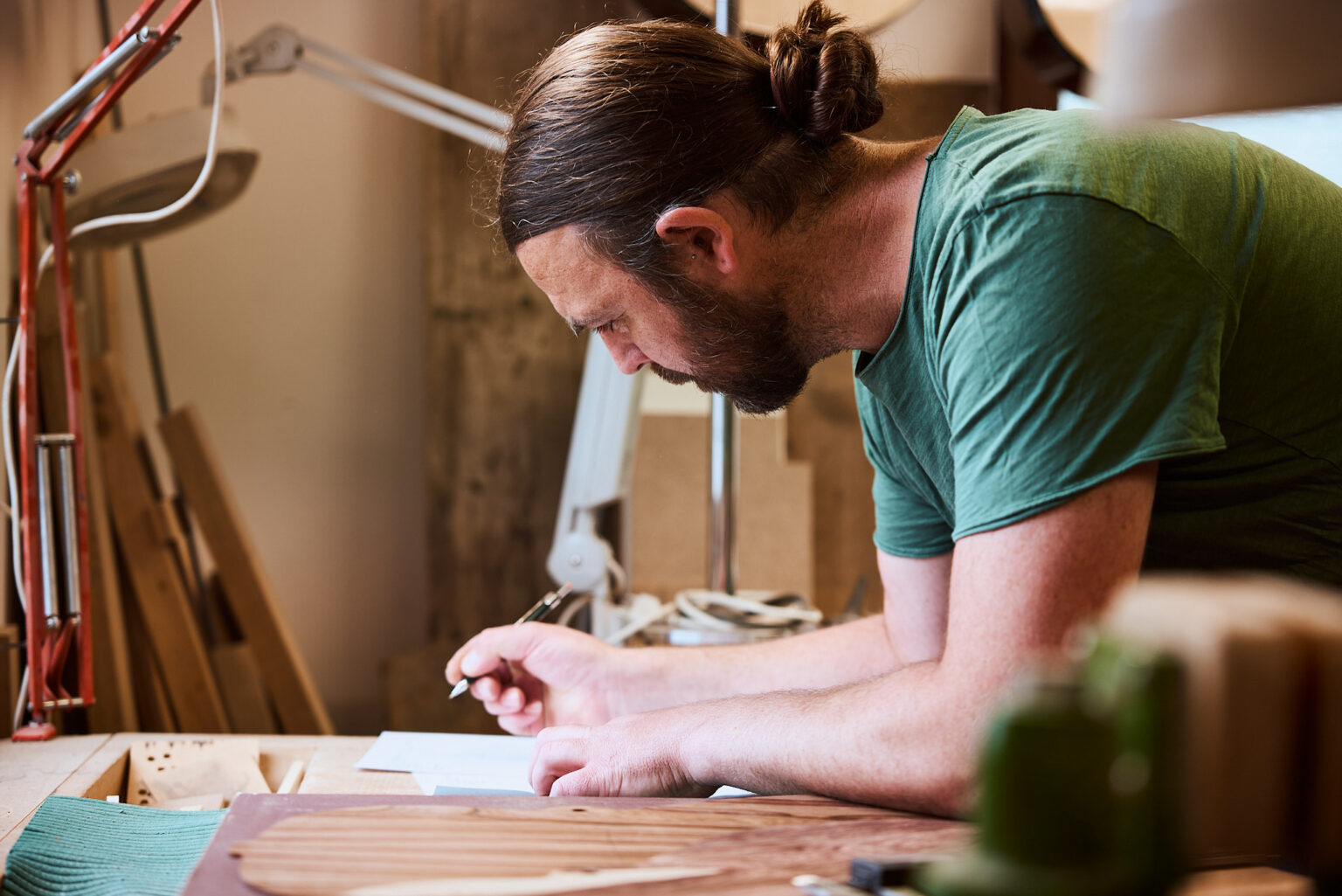 Thom Orgler, South Tyrolean luthier, sketching build notes at his workshop bench beside a spruce soundboard and bracing.